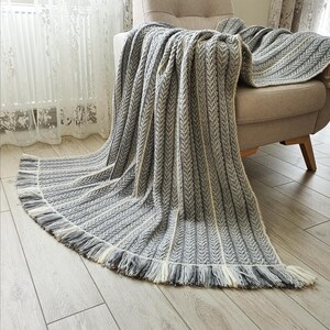 A gray and white striped throw blanket with fringe on the edges. The blanket is draped over a light gray armchair.