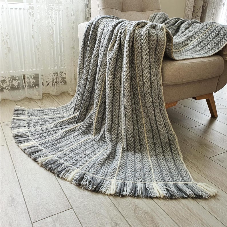 A gray and white striped throw blanket with fringe on the edges. The blanket is draped over a light gray armchair.