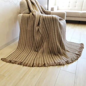 Soft crochet wool throw with neutral color palette and dense knit structure, the throw blanket is drapped over a chair.