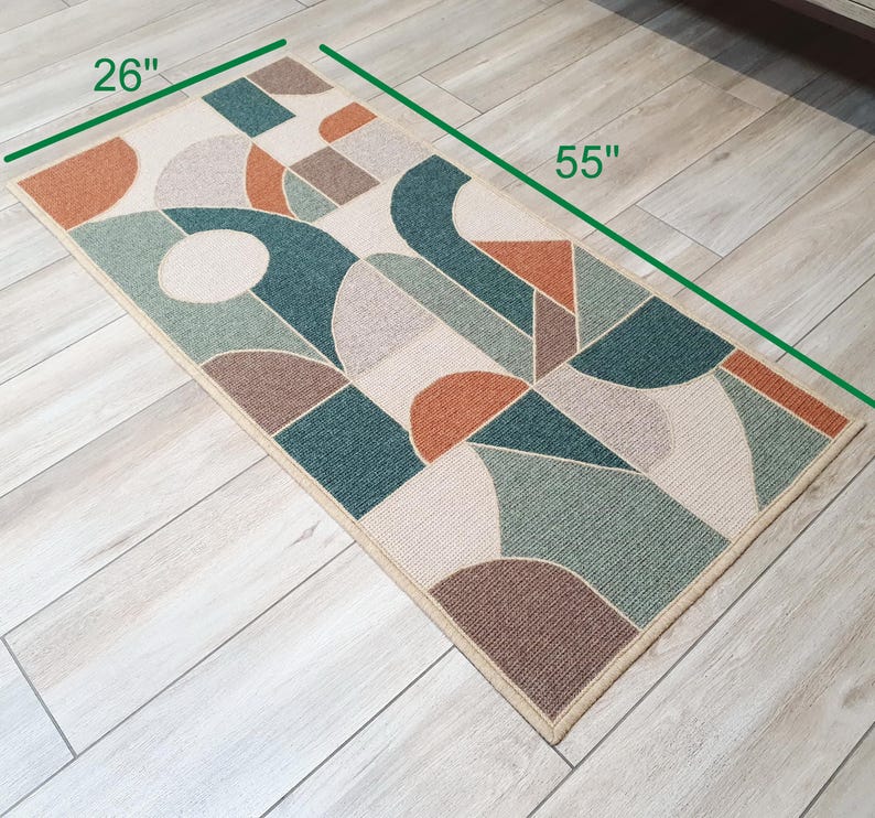 Puede incluir: Una alfombra rectangular con un patr&oacute;n geom&eacute;trico abstracto. La alfombra mide 140 cm de largo y 66 cm de ancho. Presenta formas en verde azulado, naranja, marr&oacute;n y beige. La alfombra tiene un borde beige y est&aacute; colocada sobre un suelo de madera clara.