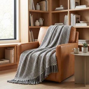 Neutral gray wool throw blanket with soft folds and heavy texture on leather chair