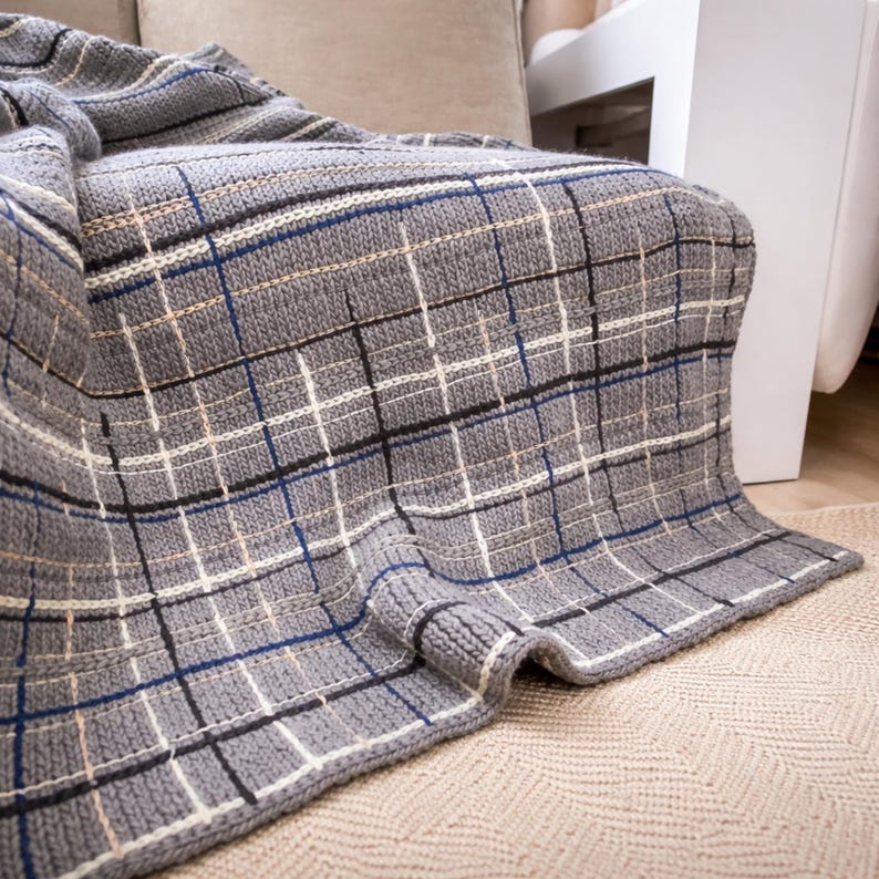 A gray and white throw blanket with a blue, white and black stripe pattern. The blanket is draped over a couch and is made of a soft, knitted fabric.