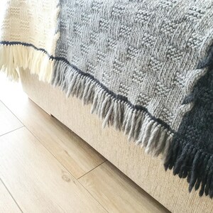 A gray and black knitted throw blanket with fringe on the edges. The blanket is draped over a light beige couch.