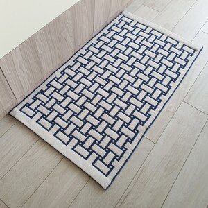 May include: A white and blue woven rug with a geometric pattern. The rug has a rectangular shape and is made of a soft, plush material.