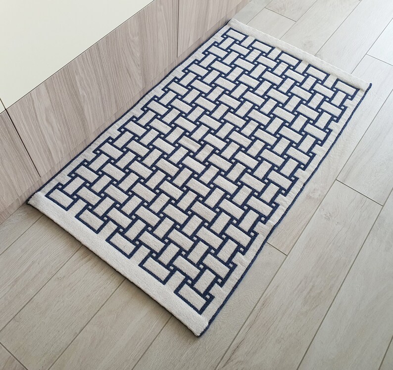 May include: A white and blue woven rug with a geometric pattern. The rug has a rectangular shape and is made of a soft, plush material.
