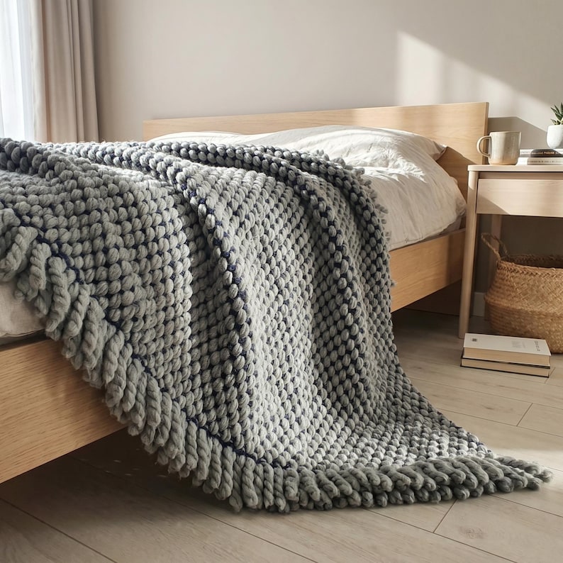 Chunky wool blanket in gray spread on a bed with natural folds and heavy textured surface.