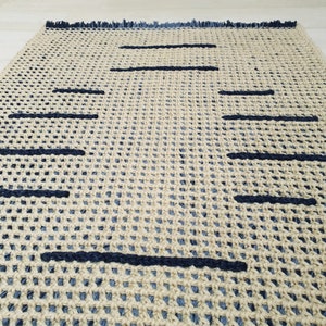 May include: A woven rug with a geometric pattern of black lines on a beige background. The rug has a fringe border.