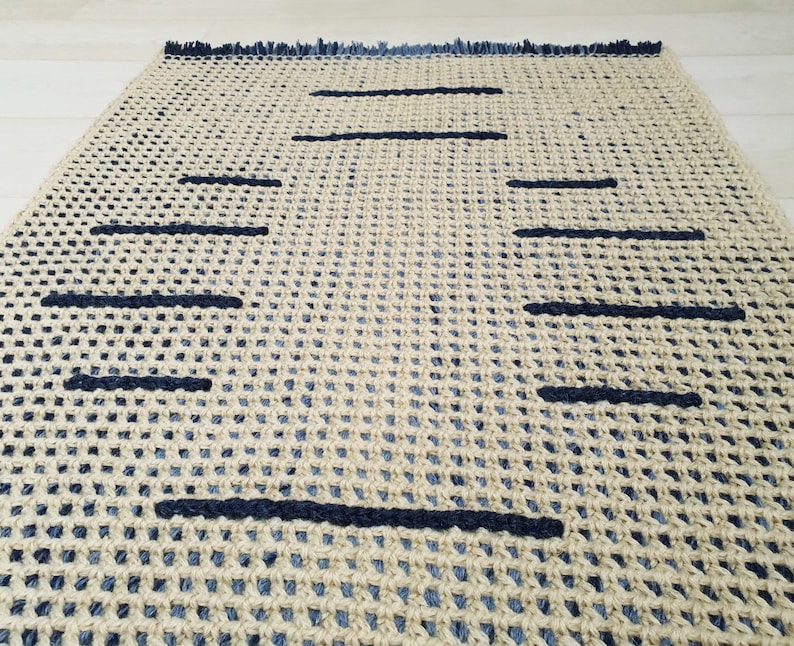 May include: A woven rug with a geometric pattern of black lines on a beige background. The rug has a fringe border.