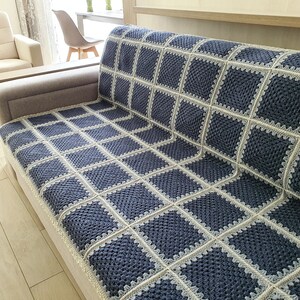 May include: A blue and white crocheted throw blanket with a square pattern. The blanket is draped over a couch.
