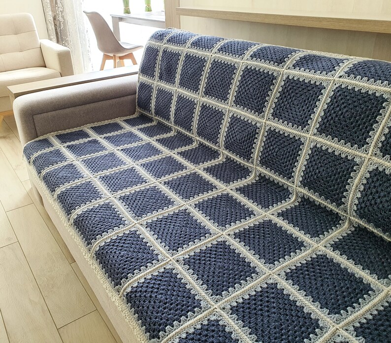 May include: A blue and white crocheted throw blanket with a square pattern. The blanket is draped over a couch.
