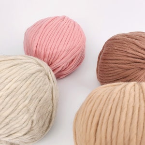 May include: Four balls of yarn in different shades of brown, beige, and pink. The yarn is thick and fluffy, perfect for knitting or crocheting.