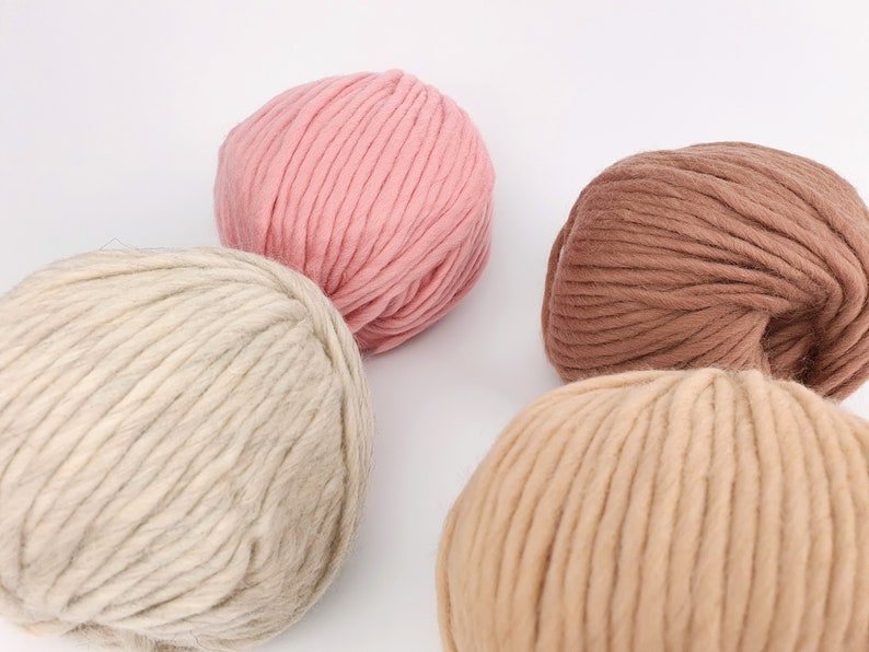 May include: Four balls of yarn in different shades of brown, beige, and pink. The yarn is thick and fluffy, perfect for knitting or crocheting.