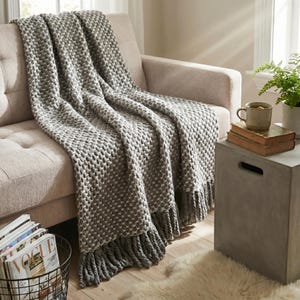 Gray wool throw blanket with large crochet pattern placed on a sofa with natural folds