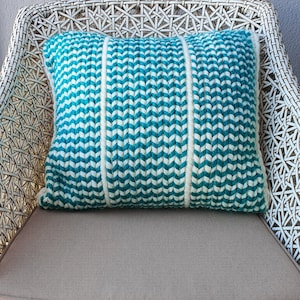 May include: A white wicker chair with a teal and white striped throw pillow. The pillow is made of a textured fabric and has a chevron pattern.