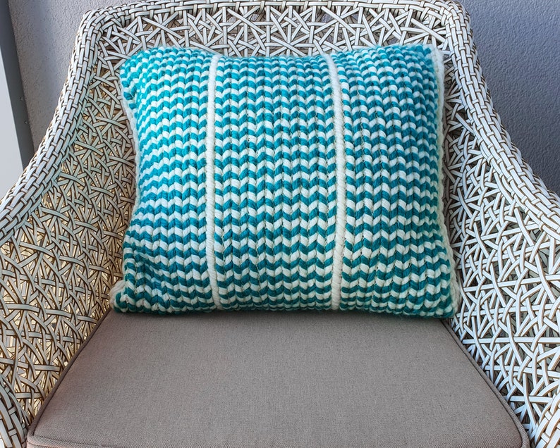 May include: A white wicker chair with a teal and white striped throw pillow. The pillow is made of a textured fabric and has a chevron pattern.