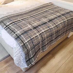 A gray and white striped throw blanket with black and blue accents. The blanket is folded and placed on a bed.