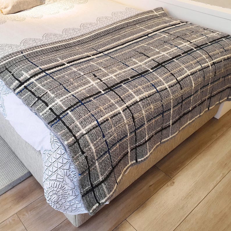 A gray and white striped throw blanket with black and blue accents. The blanket is folded and placed on a bed.