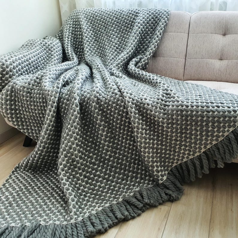 Chunky gray wool blanket draped over a sofa with visible crochet texture and thick yarn structure