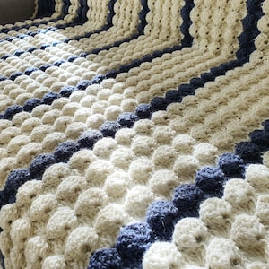 May include: A crocheted blanket with a textured pattern of white and blue circles. The blanket is made with a soft yarn and has a striped design.