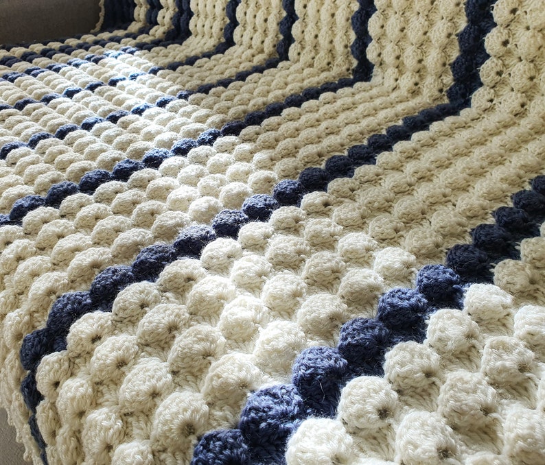May include: A crocheted blanket with a textured pattern of white and blue circles. The blanket is made with a soft yarn and has a striped design.