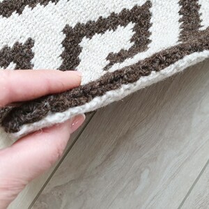 May include: Close-up of a brown and white patterned rug with a fringe edge. The rug is folded in half and being held by a hand.