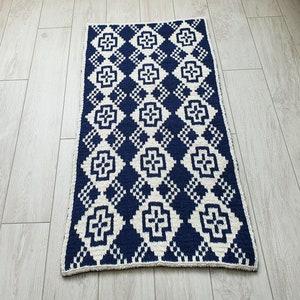 May include: A navy blue and white crocheted rug with a geometric pattern. The rug has a diamond shape with a white cross in the center of each diamond.