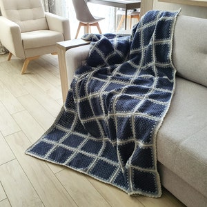 May include: A blue and white crocheted throw blanket with a square pattern draped over a gray couch.