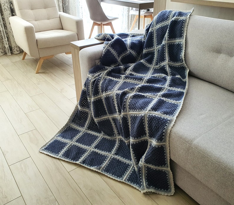 May include: A blue and white crocheted throw blanket with a square pattern draped over a gray couch.