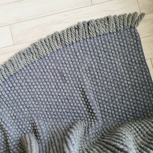 Peut inclure: Un tapis textur&eacute; gris et bleu avec une bordure &agrave; franges. Le tapis pr&eacute;sente un motif tiss&eacute; avec une texture en relief en forme de bulles. La frange est d'une nuance de gris plus claire.