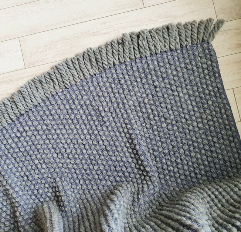 Peut inclure: Un tapis textur&eacute; gris et bleu avec une bordure &agrave; franges. Le tapis pr&eacute;sente un motif tiss&eacute; avec une texture en relief en forme de bulles. La frange est d'une nuance de gris plus claire.
