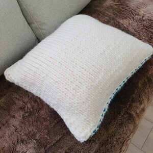 May include: White knitted throw pillow with a blue trim. The pillow is on a brown faux fur surface.