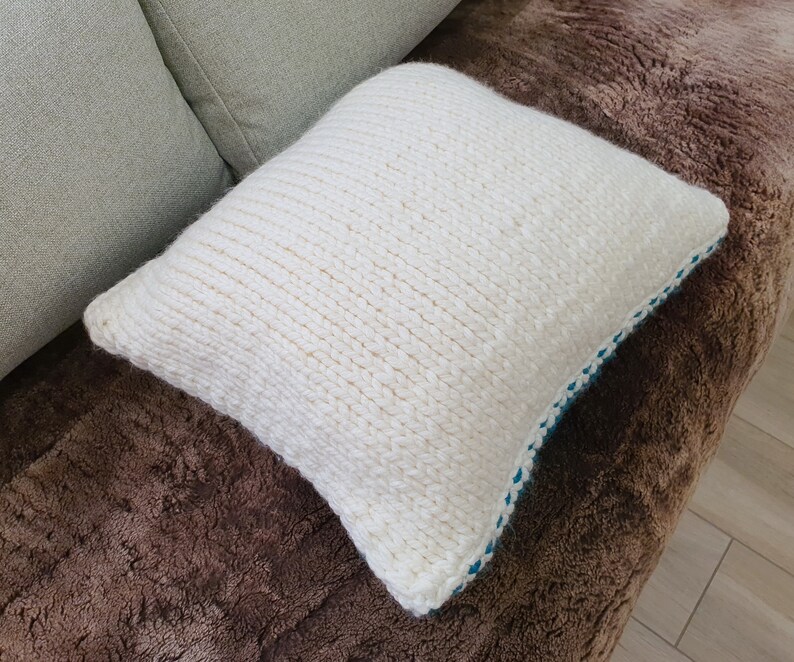 May include: White knitted throw pillow with a blue trim. The pillow is on a brown faux fur surface.
