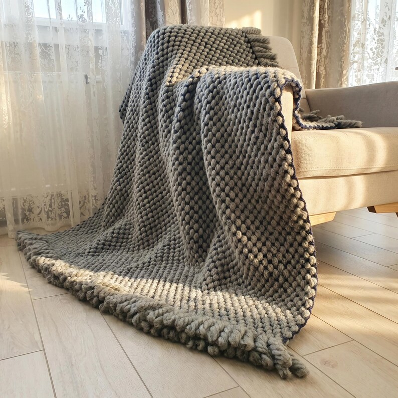 Thick wool throw draped over an armchair with visible weight and chunky knit pattern.