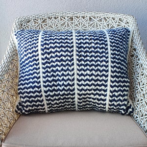 May include: A blue and white chevron patterned throw pillow with white piping. The pillow is sitting on a white wicker chair.