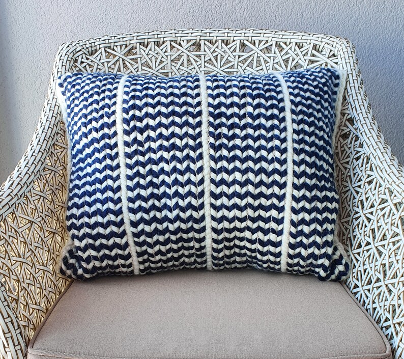 May include: A blue and white chevron patterned throw pillow with white piping. The pillow is sitting on a white wicker chair.