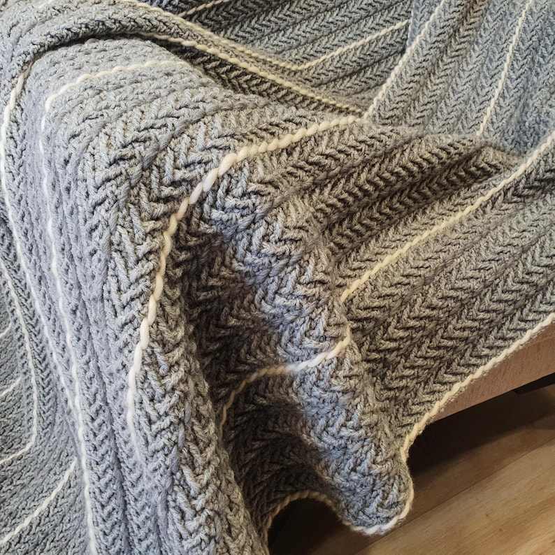 Close-up of grey crochet texture with thin white wool pinstripes and soft fringe detail. Natural wool fiber quality.