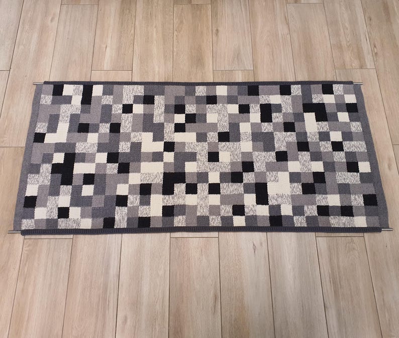 K&ouml;nnte beinhalten: Ein schwarzer, wei&szlig;er und grauer L&auml;ufer mit geometrischem Muster. Der L&auml;ufer ist aus einem weichen, gewebten Material gefertigt und hat einen dezenten Glanz.