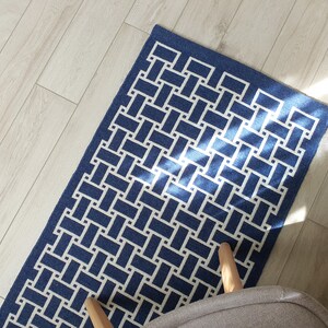 May include: A blue and white geometric patterned rug with a woven design. The rug is on a light wood floor.
