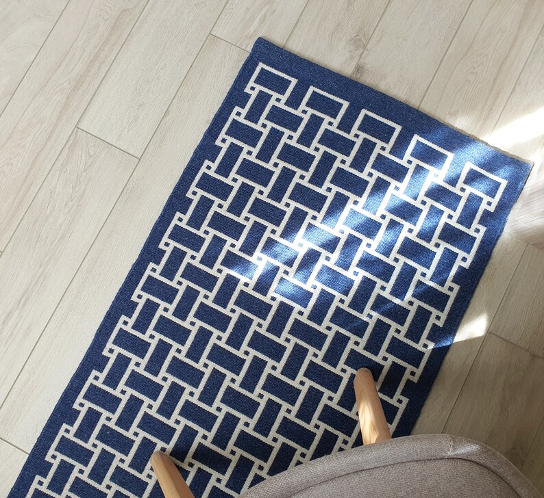 May include: A blue and white geometric patterned rug with a woven design. The rug is on a light wood floor.