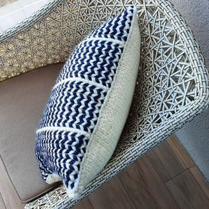 May include: A white wicker chair with a blue and white patterned throw pillow. The pillow has a chevron pattern and is made of a soft, woven fabric.