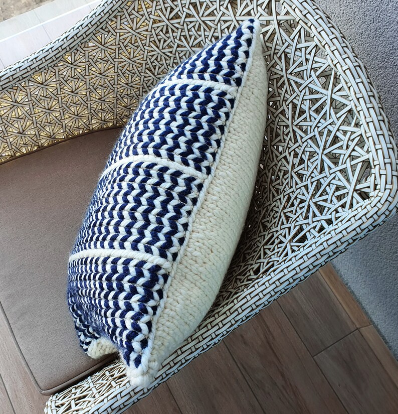 May include: A white wicker chair with a blue and white patterned throw pillow. The pillow has a chevron pattern and is made of a soft, woven fabric.