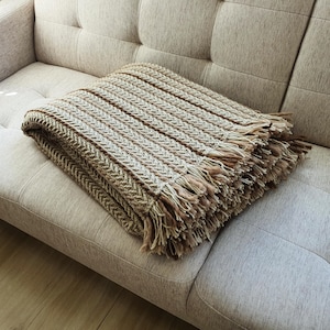 Folded beige crochet wool blanket placed on a couch, large textured knit throw with natural folds.