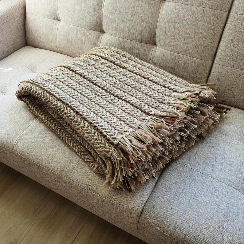Folded beige crochet wool blanket placed on a couch, large textured knit throw with natural folds.