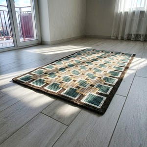 Full view of handmade wool rug in Beige, Brown, Green and Teal, geometric pattern, rectangular shape on light floor in evening light.