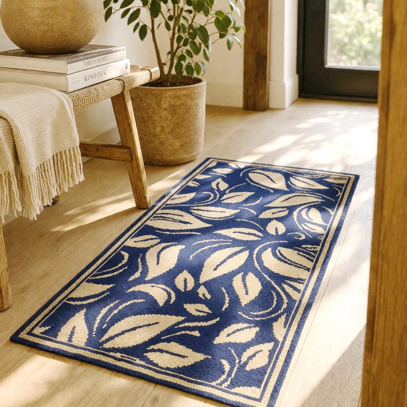 A hand-woven wool rug with embroidered yellow leaves on a dark blue background lies on the light wooden floor in the cottage's entryway.