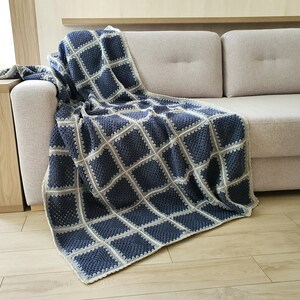 May include: A crocheted throw blanket in a blue and white color scheme with a square pattern. The blanket is draped over a light gray sofa.