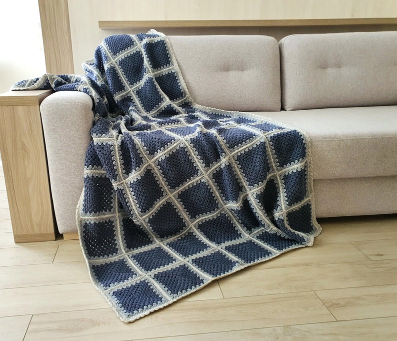 May include: A crocheted throw blanket in a blue and white color scheme with a square pattern. The blanket is draped over a light gray sofa.