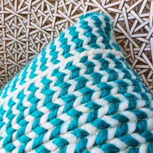 May include: A close-up of a turquoise and white woven throw pillow. The pillow is made of a thick, textured fabric and has a chevron pattern.