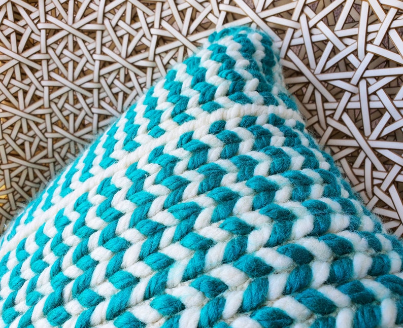 May include: A close-up of a turquoise and white woven throw pillow. The pillow is made of a thick, textured fabric and has a chevron pattern.