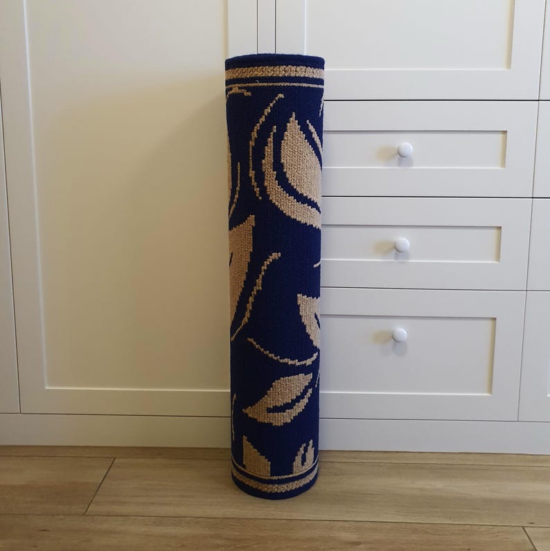 A rolled-up blue and beige patterned rug with a floral design. The rug is rolled up and standing upright on a wooden floor.